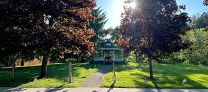 Photo of a bandstand on green grass with trees and the sun setting behind.